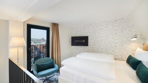 Et hotelværelse med en seng, en stol, et skrivebord og et vindue med udsigt til bygninger.