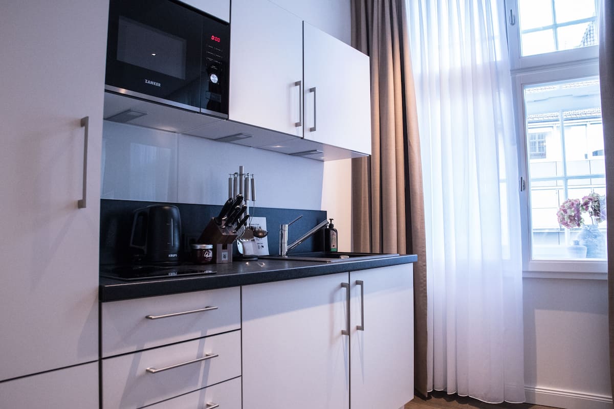 Una cocina moderna con armarios blancos, encimera negra y una ventana con cortinas.