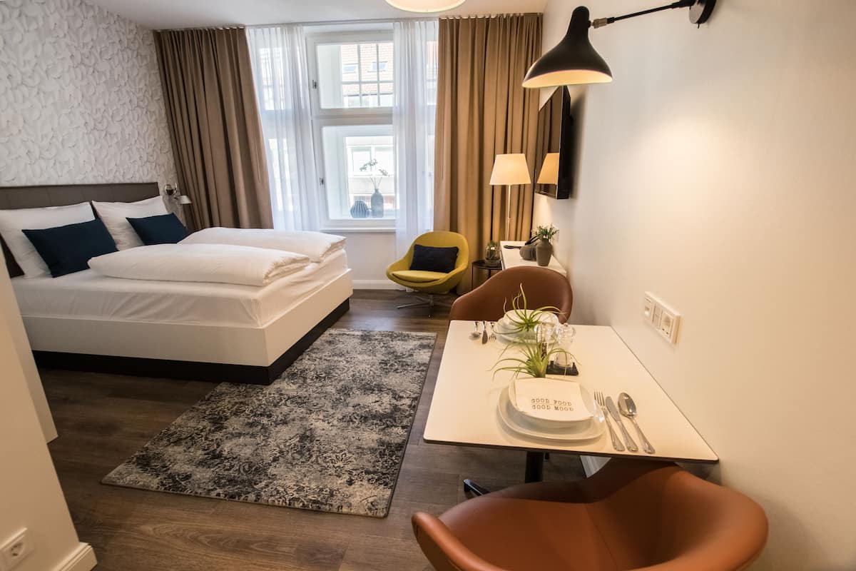 Una habitación de hotel con una cama, una mesa de comedor con una planta, una silla y una lámpara.