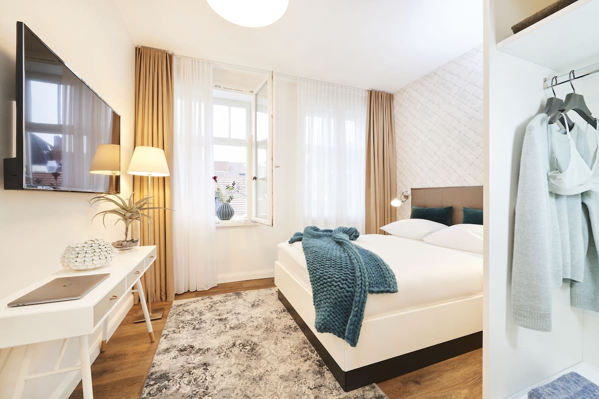 Una habitación de hotel moderna con cama, mesita de noche, lámpara y vistas al exterior.