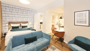 Et moderne soveværelse med en stor seng, en blå sofa og et spiseområde med bord og stole.