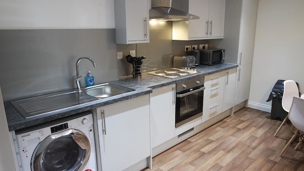 A compact kitchen with a washing machine, a sink, a toaster, and a microwave. - Jaylets Premier Apartments, Leicester. (Leicester)