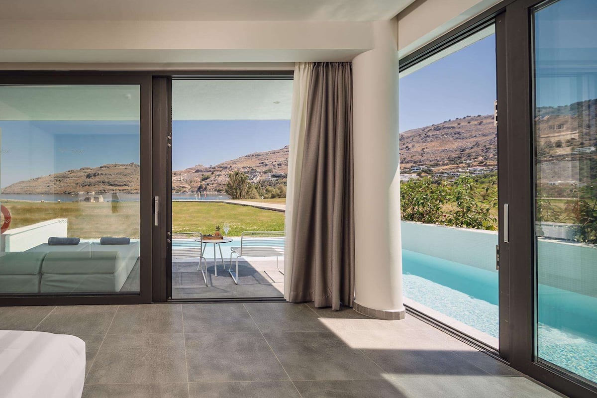 A modern hotel room with a large sliding glass door leading to a private pool area.
