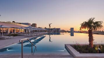 A swimming pool with lounge chairs and umbrellas, surrounded by buildings and palm trees.