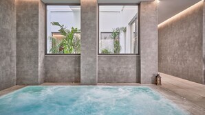 Un cuarto de spa con una bañera grande, paredes de concreto y ventanas amplias con vista a un jardín.