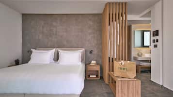 Une chambre d’hôtel moderne avec un grand lit, une cloison en bois, une petite table de chevet et une salle de bain visible au fond.