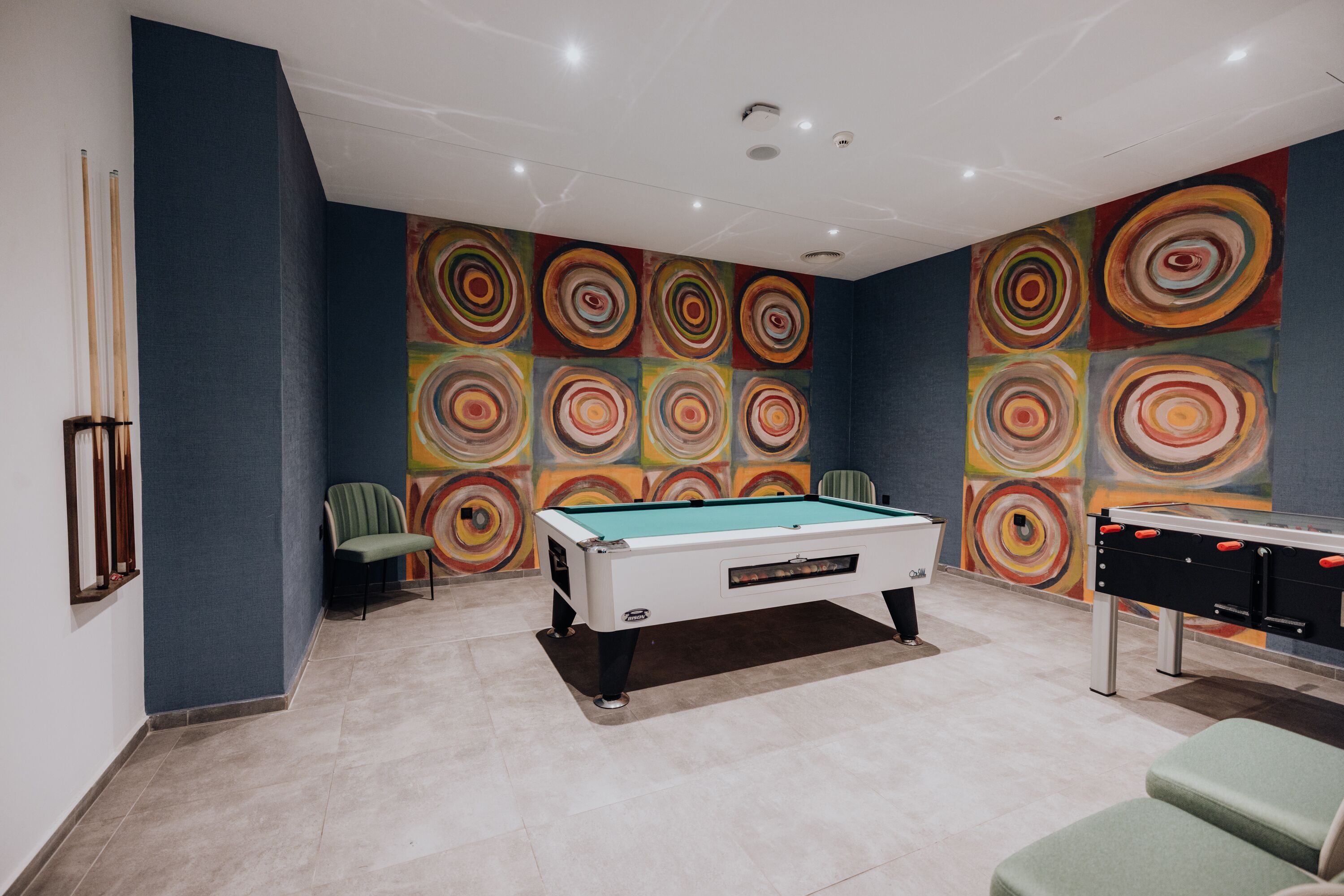 A pool table in a room with a colorful circular mural on the wall.