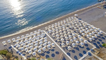 Une vue aérienne d’une plage avec des rangées de parasols et de chaises longues.