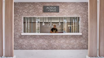 A reception area with a brick wall, a sign reading "ACQUA + SALE", and a window with hanging lights.