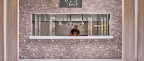 A reception area with a brick wall, a sign reading "ACQUA + SALE", and a window with hanging lights.