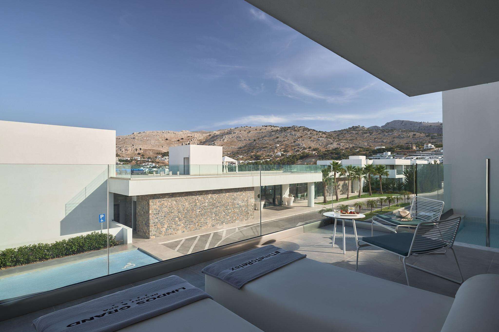 A modern outdoor lounge area with a pool, seating, and a view of a hillside town.