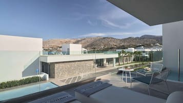 Un área lounge moderna al aire libre con piscina, asientos y vistas a un pueblo en la ladera.