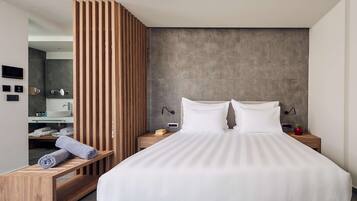 A modern bedroom with a large bed, wooden bedside tables, a built-in bench with towels, and a concrete accent wall.