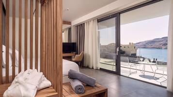 Ein Hotelzimmer mit einem Bett, einem Fernseher, einem Nachttisch aus Holz mit Handtüchern und einem Balkon mit Tisch und Stühlen mit Blick auf ein Gewässer.