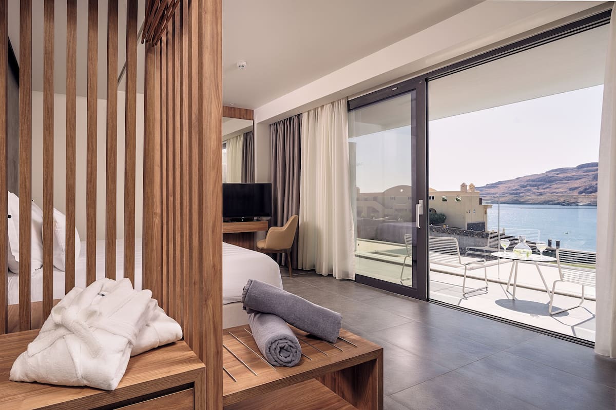 A modern hotel room with a wooden partition, a bed, a TV, and a balcony with a table and chairs.
