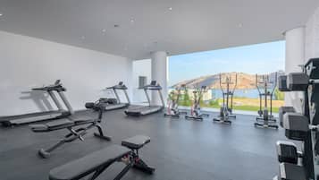 A modern gym with treadmills, elliptical machines, and weight benches, featuring a large window with a mountain view.