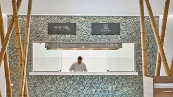 A reception area with a geometric patterned wall, two signs for 'Yume MOU' and 'Takara' restaurants, and a counter with a person behind it.