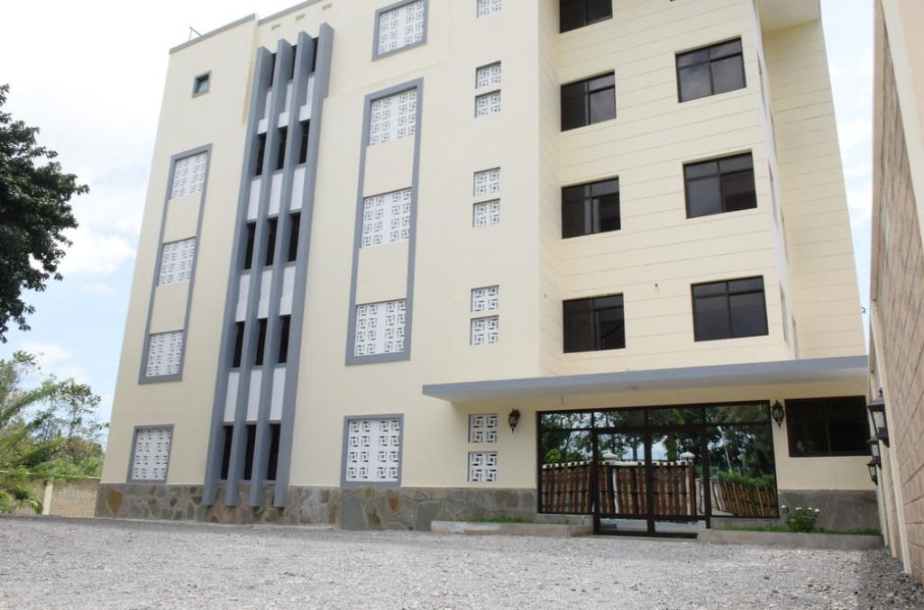 A multi-story building with a beige facade, vertical slits on the facade, and a covered entrance area.