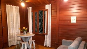 Une pièce chaleureuse avec une table ronde, deux tabourets, un canapé gris et une fenêtre ornée de barreaux en fer décoratifs.