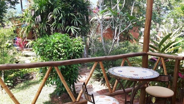Une terrasse en bois avec une table ronde et deux chaises, entourée d’une végétation luxuriante et de diverses plantes.
