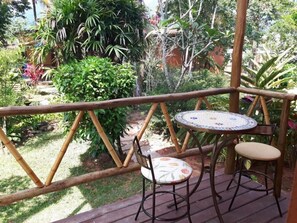 A wooden deck with a round table and two chairs, surrounded by lush greenery and a variety of plants. - Canto Bella Terra Pousada (Ilhabela)
