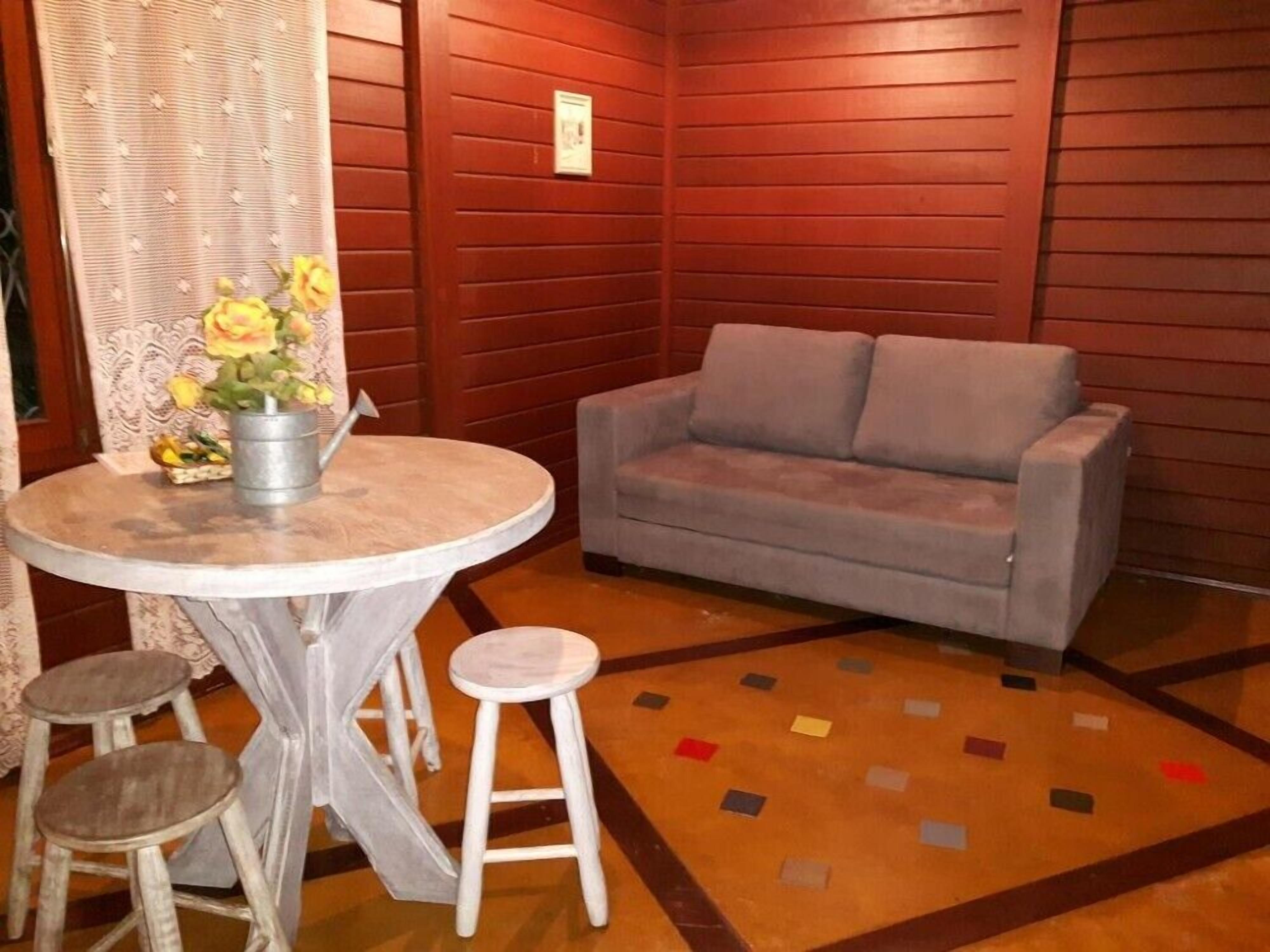 A room with a grey sofa, a round table with two stools, and a patterned rug.