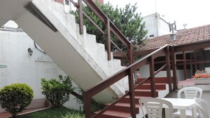 A staircase with a brown handrail leading to a landing, surrounded by potted plants and white plastic chairs. - Hotel Aldea Marina (Villa Gesell)