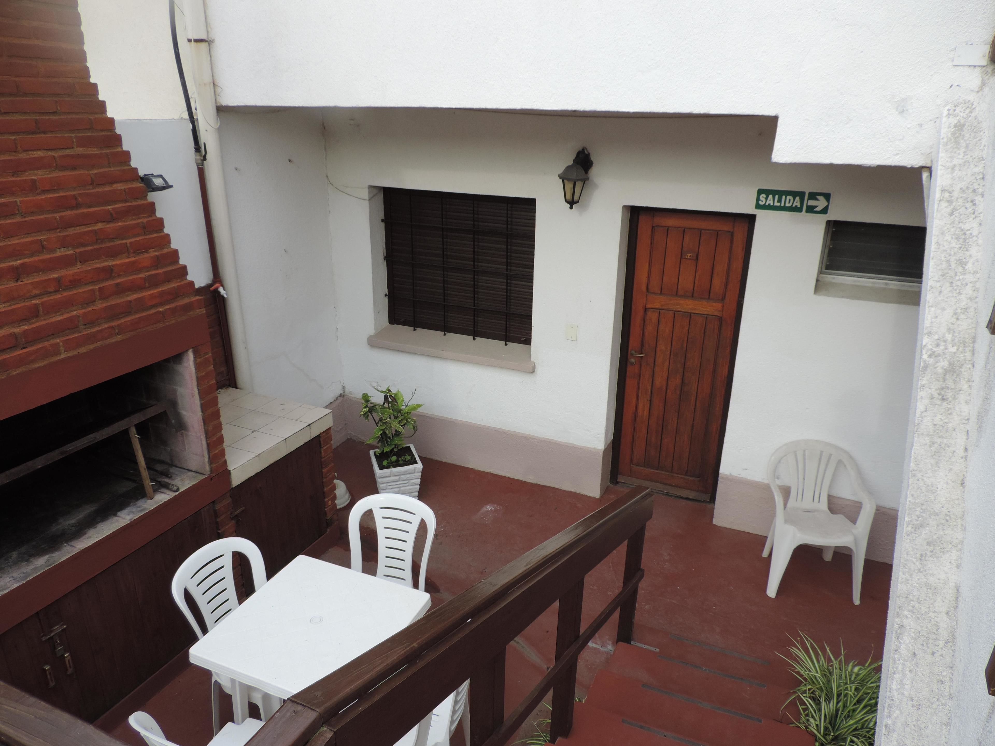 A courtyard with a wooden table and chairs, a potted plant, a door, and a window with blinds.