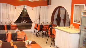A restaurant with orange and white decor, including tables and chairs, a bar area, and a view through a large window. - Hotel Aldea Marina (Villa Gesell)