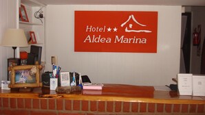 A reception desk with a sign reading "Hotel Aldea Marina" and a brick wall behind it. - Hotel Aldea Marina (Villa Gesell)