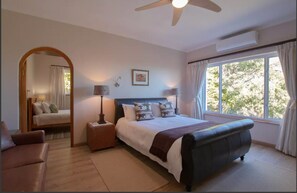 A bedroom with a bed, nightstands, a mirror, a ceiling fan, and a window with curtains.