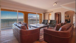 A spacious living room with leather sofas, a glass coffee table, and a view of a cityscape through large windows. - Bikini Beach Beauty (Cape Town)