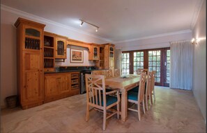 A spacious kitchen with wooden cabinets, a dining table with chairs, and large windows allowing natural light.