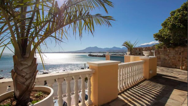 A balcony with a view of the sea and mountains, a palm tree, and a stone wall. - Bikini Beach Beauty (Cape Town)