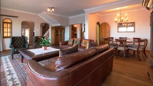 A spacious living room with a leather sofa, a dining table with chairs, and a chandelier. - Bikini Beach Beauty (Cape Town)