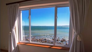 A room with a large window overlooking a rocky beach and the sea. - Bikini Beach Beauty (Cape Town)