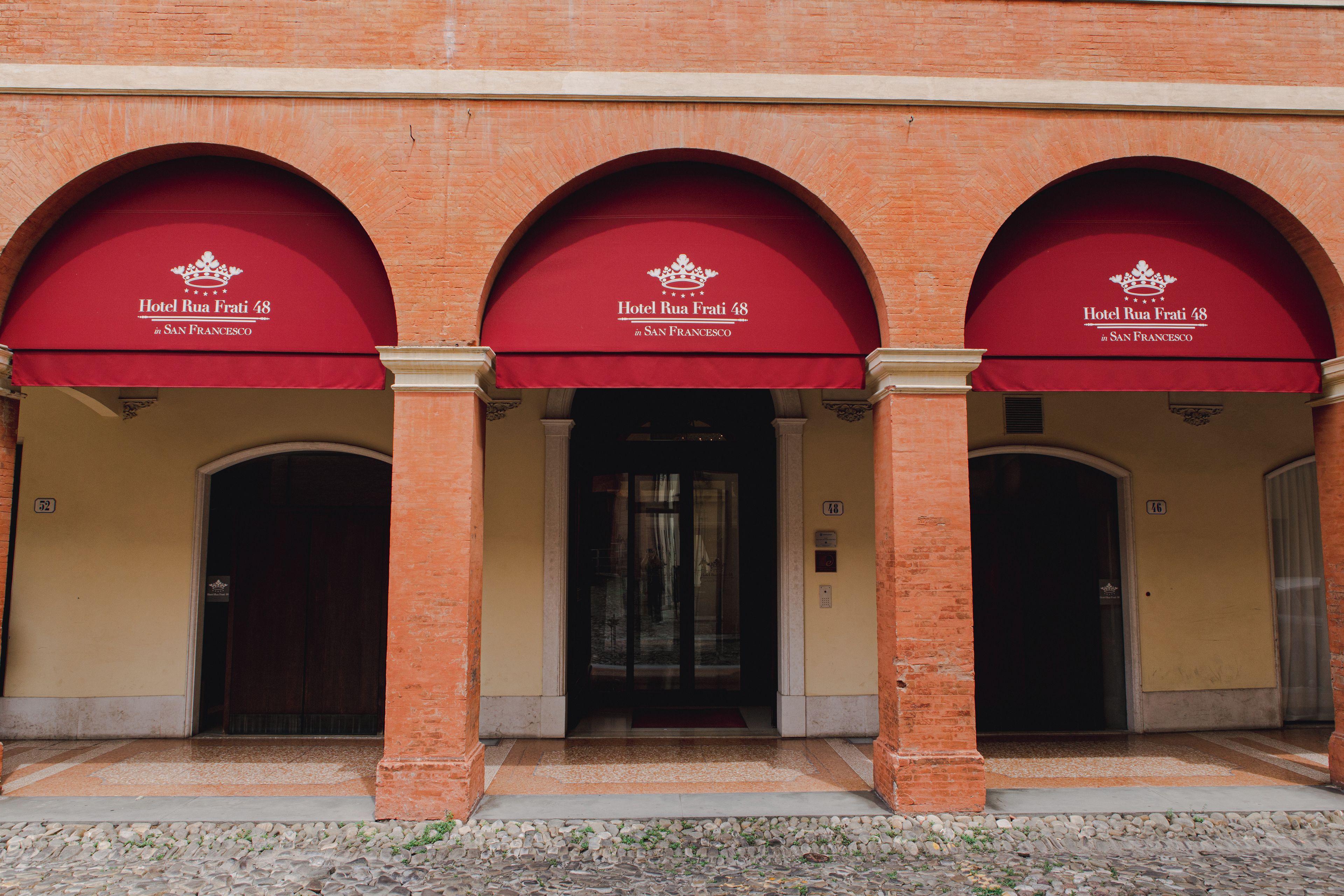 Fachada de edificio con tres entradas en arco, cada una con un toldo rojo que muestra el nombre 'Hotel Rua Frati 48 en San Francisco'.
