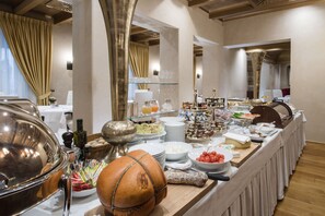 A buffet setup with various food items and beverages, including a large metal bowl, a wooden bowl, and several plates and bowls with food.