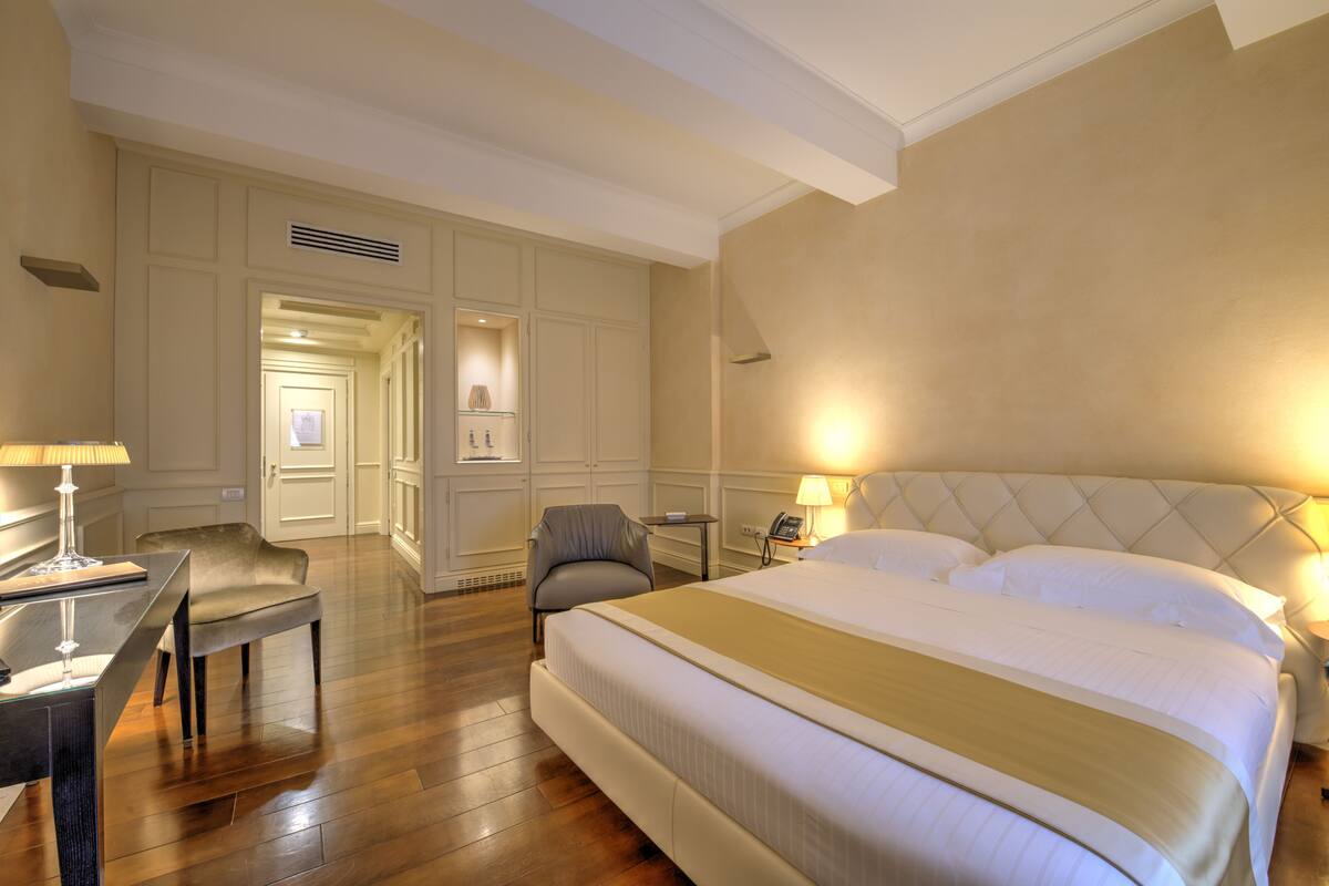 A hotel room with a large bed, a desk, a chair, and a small table.
