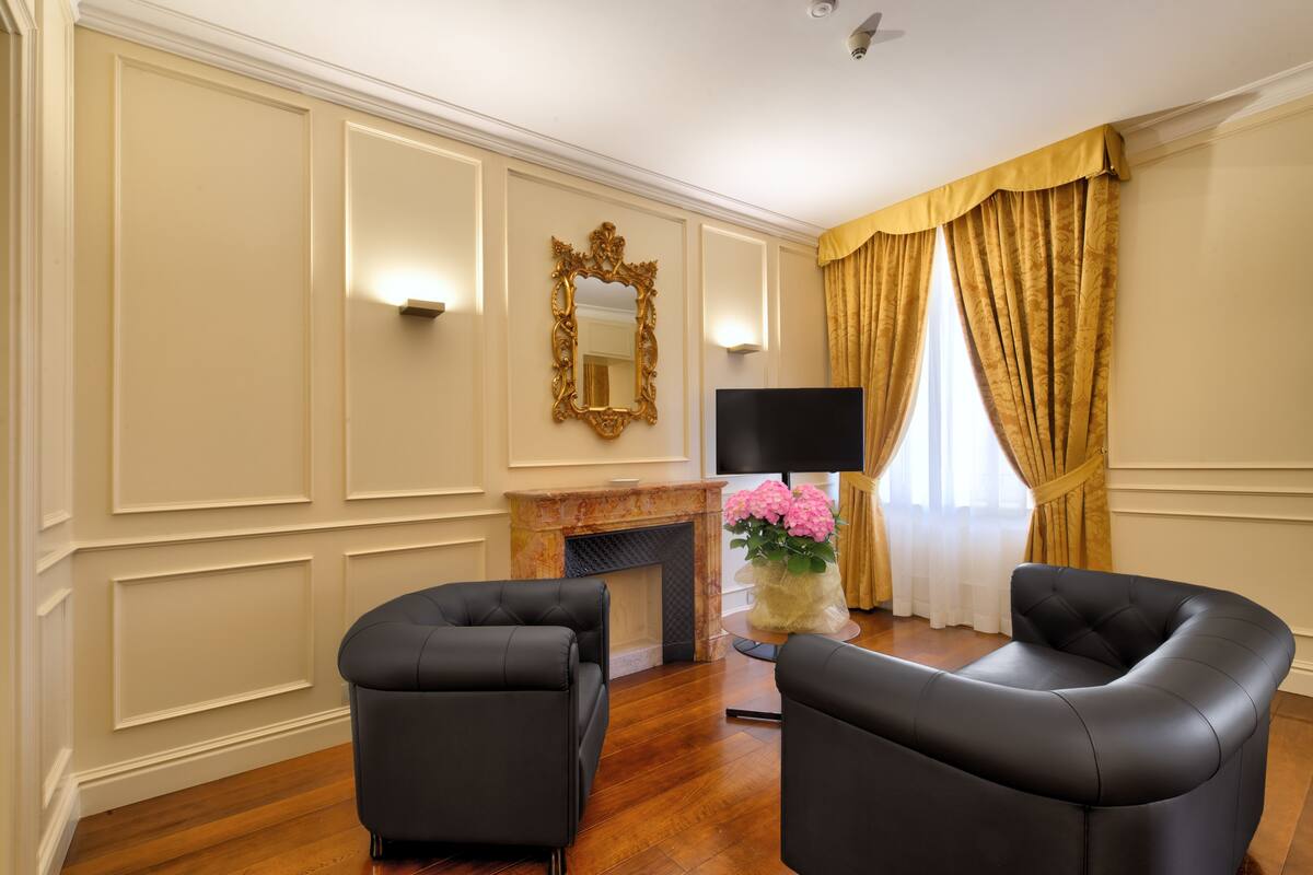 A room with two black leather armchairs, a fireplace, a large mirror, and a flat-screen TV.