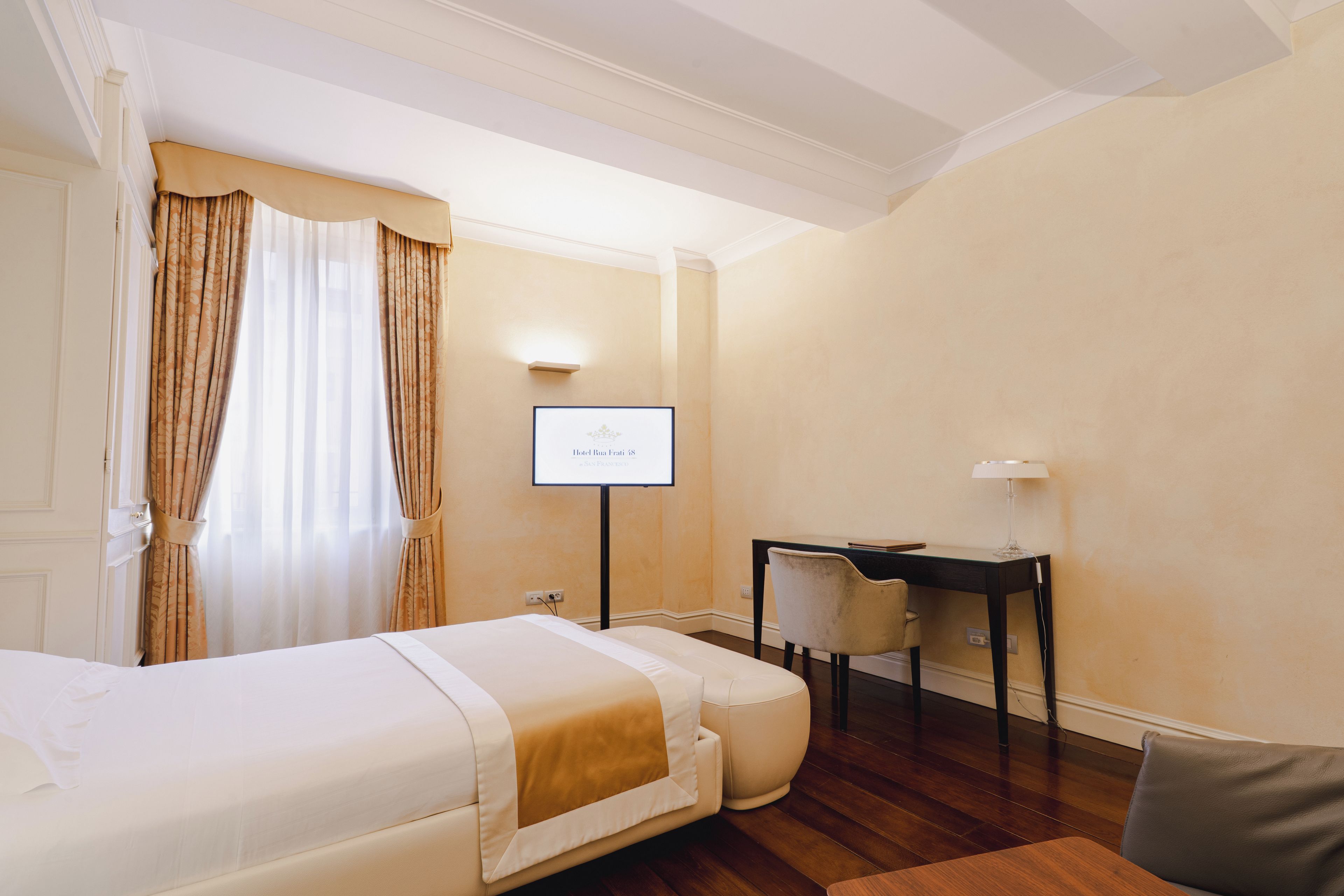 A hotel room with a bed, a desk, a chair, and a television displaying 'Hotel Rua Frei 48'.