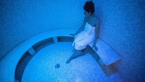 A person sitting on a bench in a blue-lit indoor pool area. - Hotel Rua Frati 48 in San Francesco (Modena)