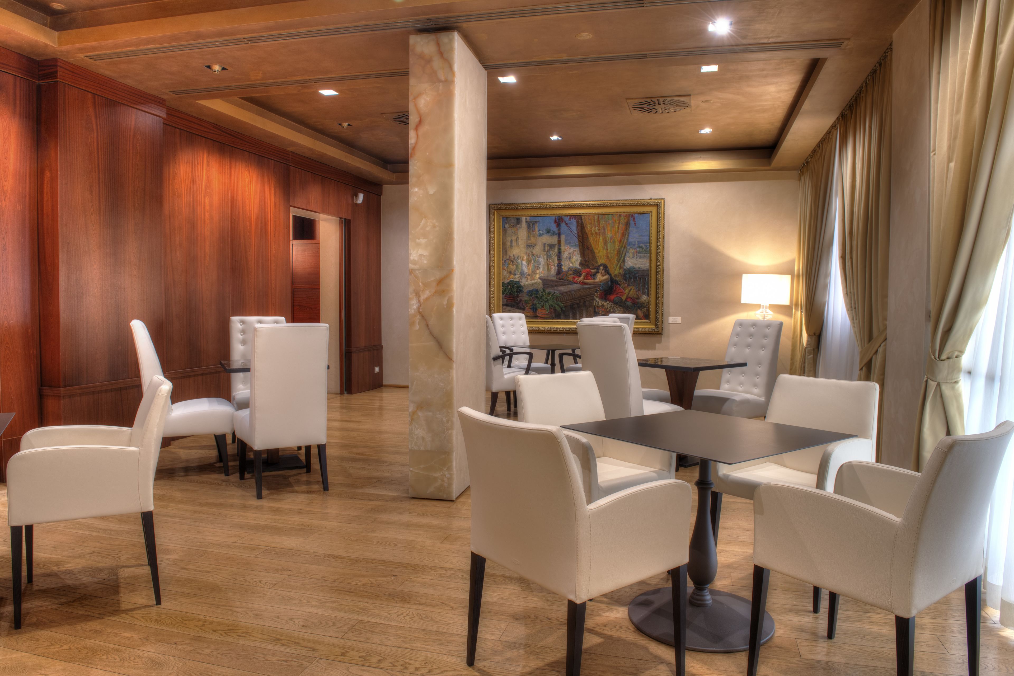 Een hotellobby met een wand van houtpanelen, een marmeren kolom, een schilderij en een tafel met stoelen.