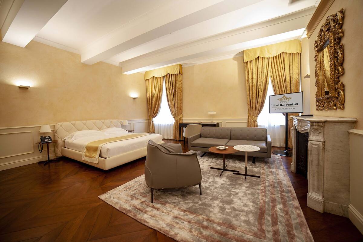 A hotel room with a bed, sofa, armchair, and a fireplace.