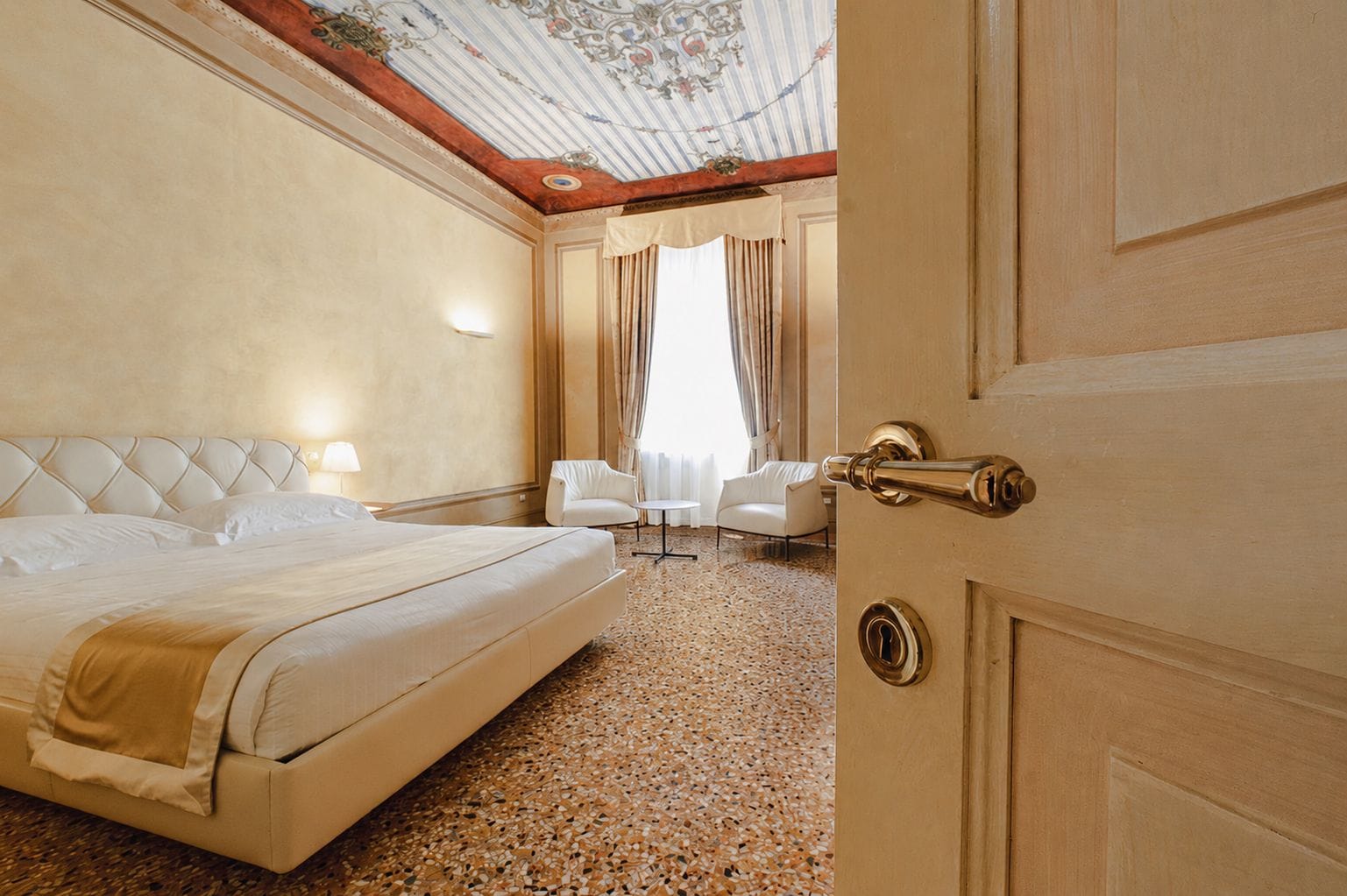 Une chambre d’hôtel avec un grand lit, un coin salon comprenant une chaise et une table, et une porte dotée d’un trou de serrure.