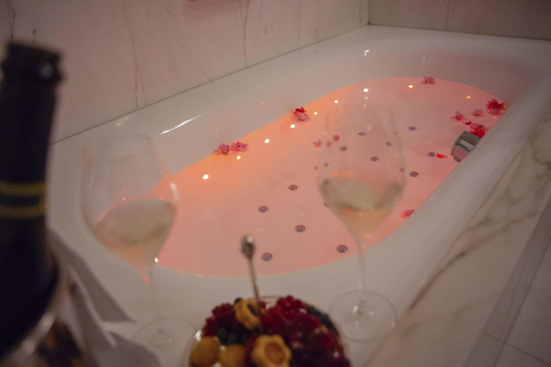 A bathtub with water, rose petals, and a glass of wine.