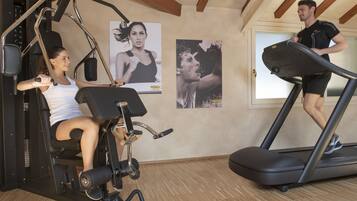 Uma academia com equipamentos de ginástica, esteira e piso de madeira.