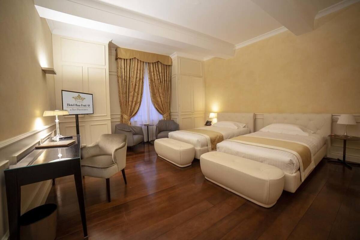 A hotel room with a large bed, two bedside tables, a desk, a chair, and a small table with a lamp.