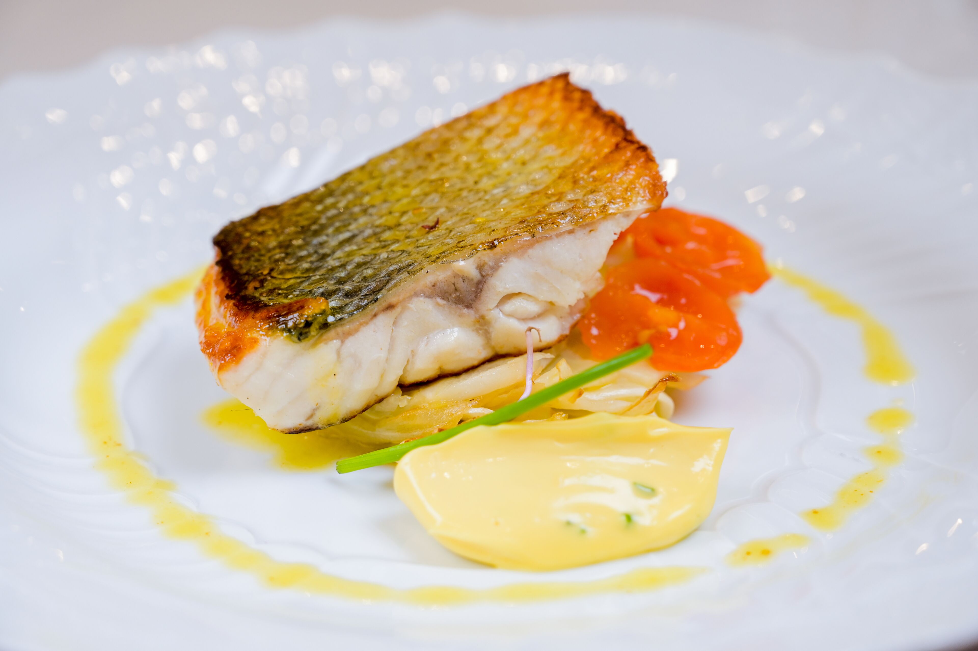 Un piatto bianco con un pezzo di pesce, un cucchiaio di salsa e una guarnizione arancione.