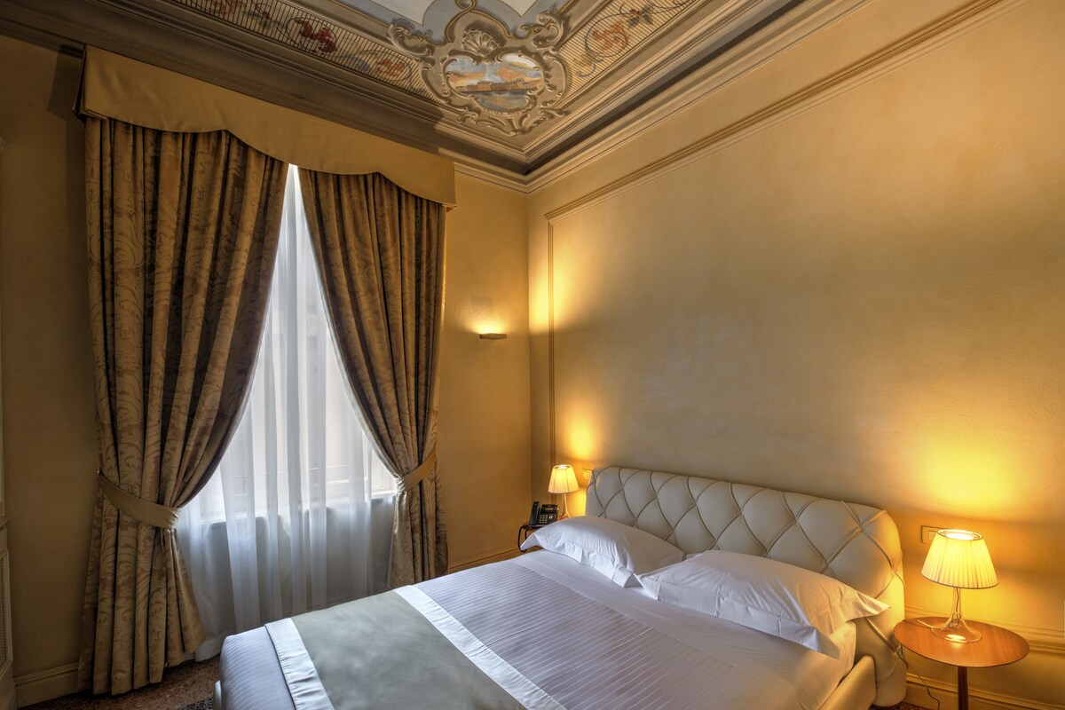 A hotel room with a large bed, two bedside lamps, and a decorative ceiling.